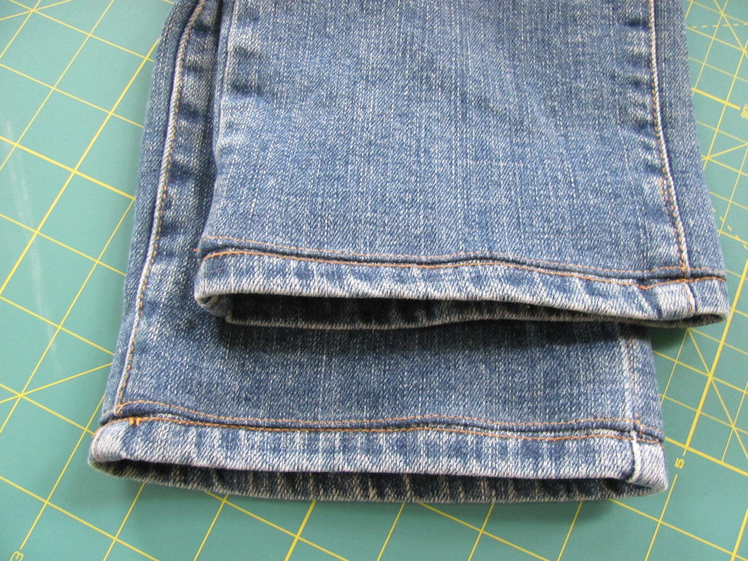Photo of hemmed jeans on top of a green gridded cutting board for sewing.